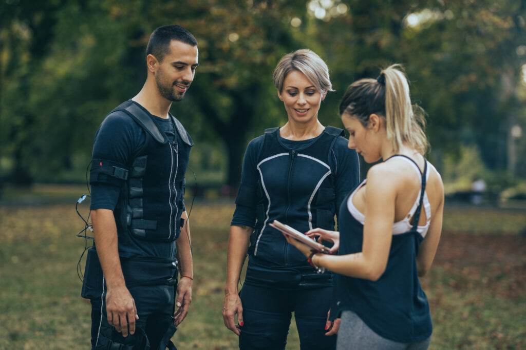 A man in a wireless EMS suit next two two women in fitness attire.