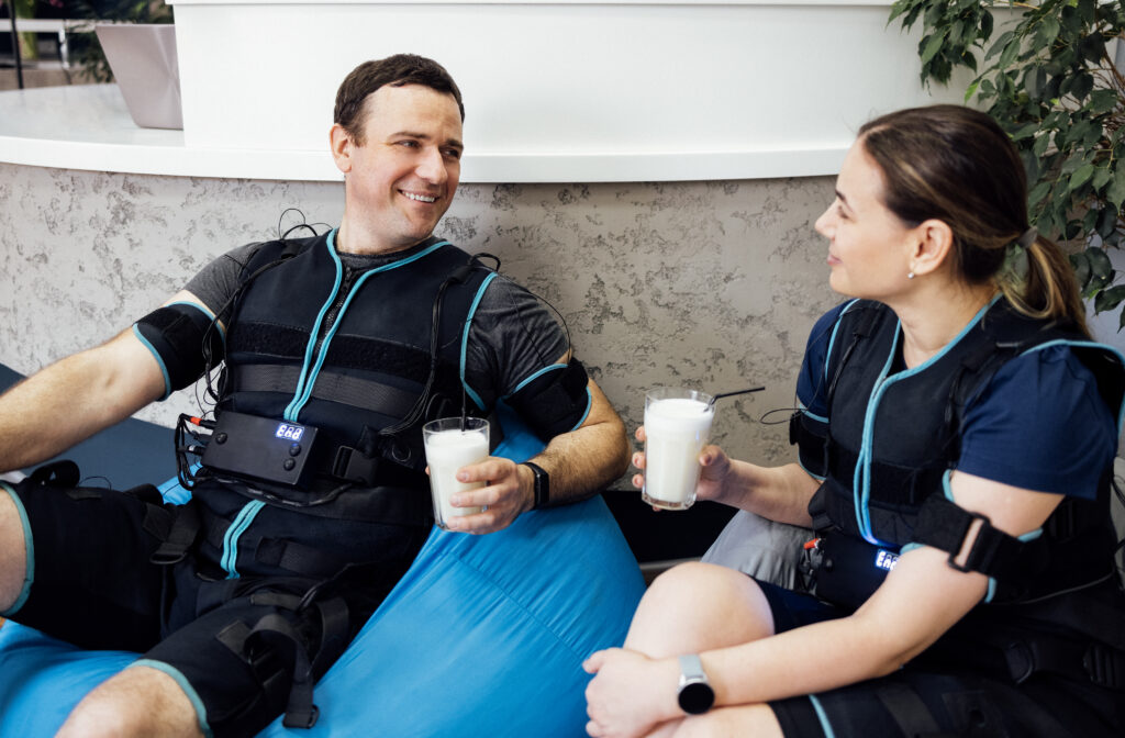 Two clients relaxing with protein shakes after an EMS training session, a good example of how long is EMS training recovery time.