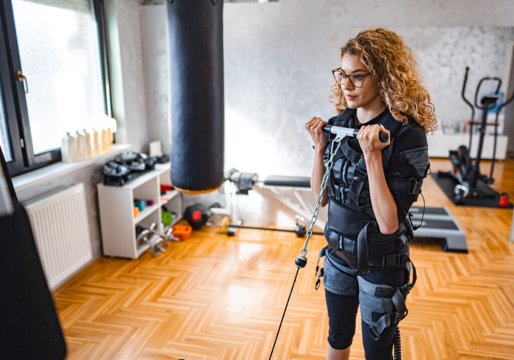 Woman doing bicep curls in an EMS training suit, illustrating how does EMS build muscle when paired with voluntary movement